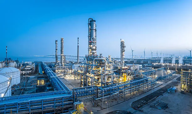 Refinery towers, blue pipes and access roads beneath a clear blue sky