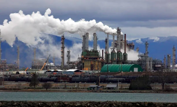 An industrial facility with stacks and white plumes beyond a stretch of water