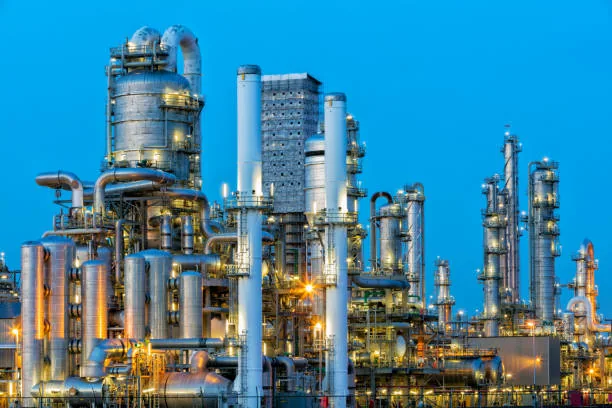 A close view of metal refinery columns and pipes against a blue sky