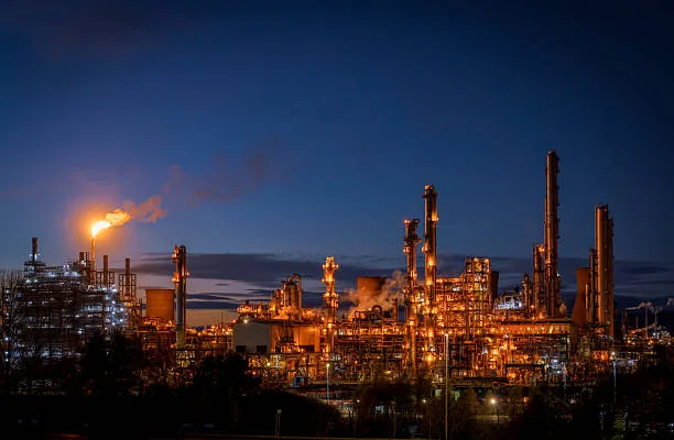 A lit flare and illuminated refinery columns against a dark night sky