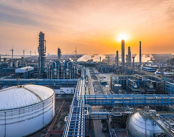 Large storage tanks and parallel pipe racks leading toward industrial towers at sunset